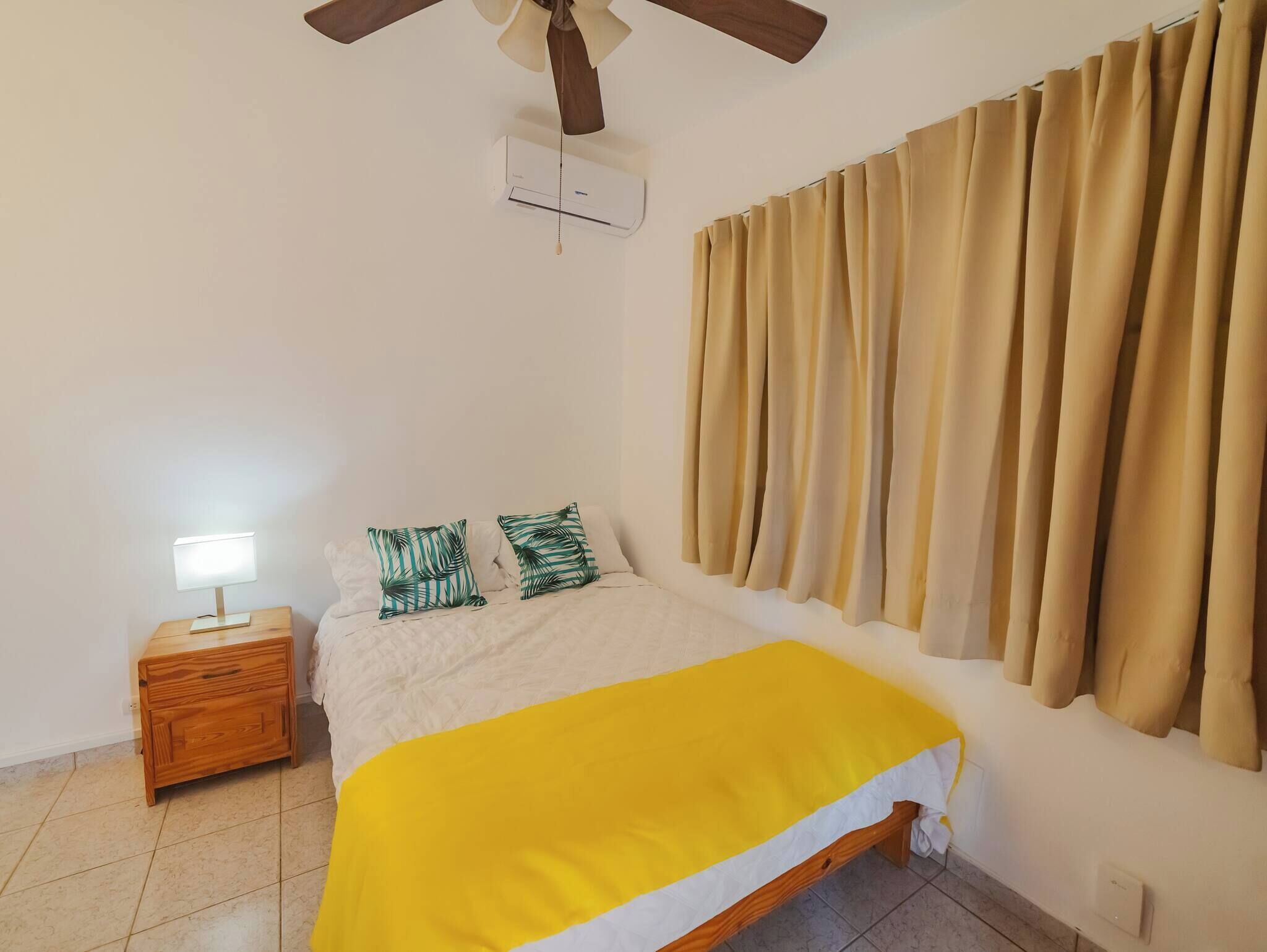 A bedroom with a bed, a nightstand, a ceiling fan, and a window with curtains.