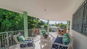 A covered balcony with wicker furniture, a small table, and a view of greenery. - 7br Massive Villa In Sosúa - 2mins From Nightlife! (Sosúa)