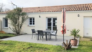 Ein Haus mit Ziegeldach, einer Terrasse mit Tisch und Stühlen und einem Blumentopf.