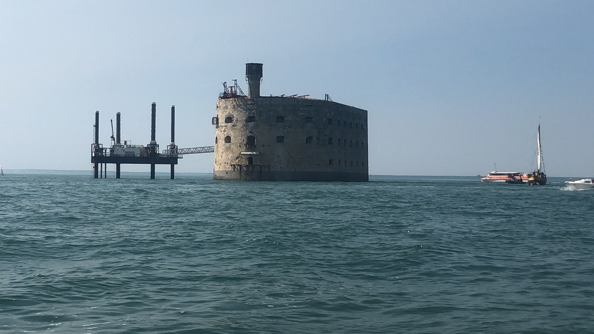 Um edifício grande e isolado numa pequena ilha, com um cais que se projeta para a água.