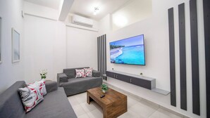 A modern living room with a grey sofa, a wooden coffee table, a flat-screen TV, and a wall-mounted air conditioner. - Cozy 1 Bedroom Apartment in Heart of Sosúa (Sosúa)