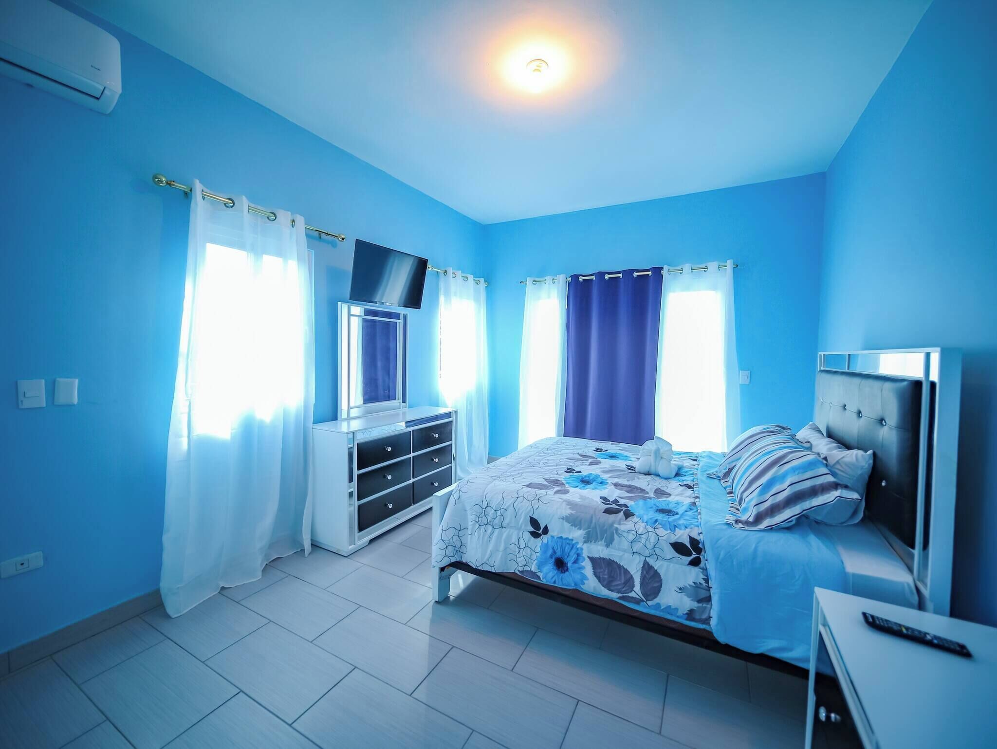 A bedroom with a bed, a TV, a dresser, and a ceiling light.