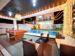 Un espace piscine équipé d’une table de billard, de chaises longues et de guirlandes lumineuses.