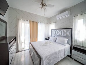 Une chambre à coucher comprenant un lit, un ventilateur de plafond, un appareil de climatisation et une table de chevet.