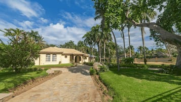 Une maison avec un chemin de pierre menant à l’entrée, entourée d’une végétation luxuriante et de palmiers.