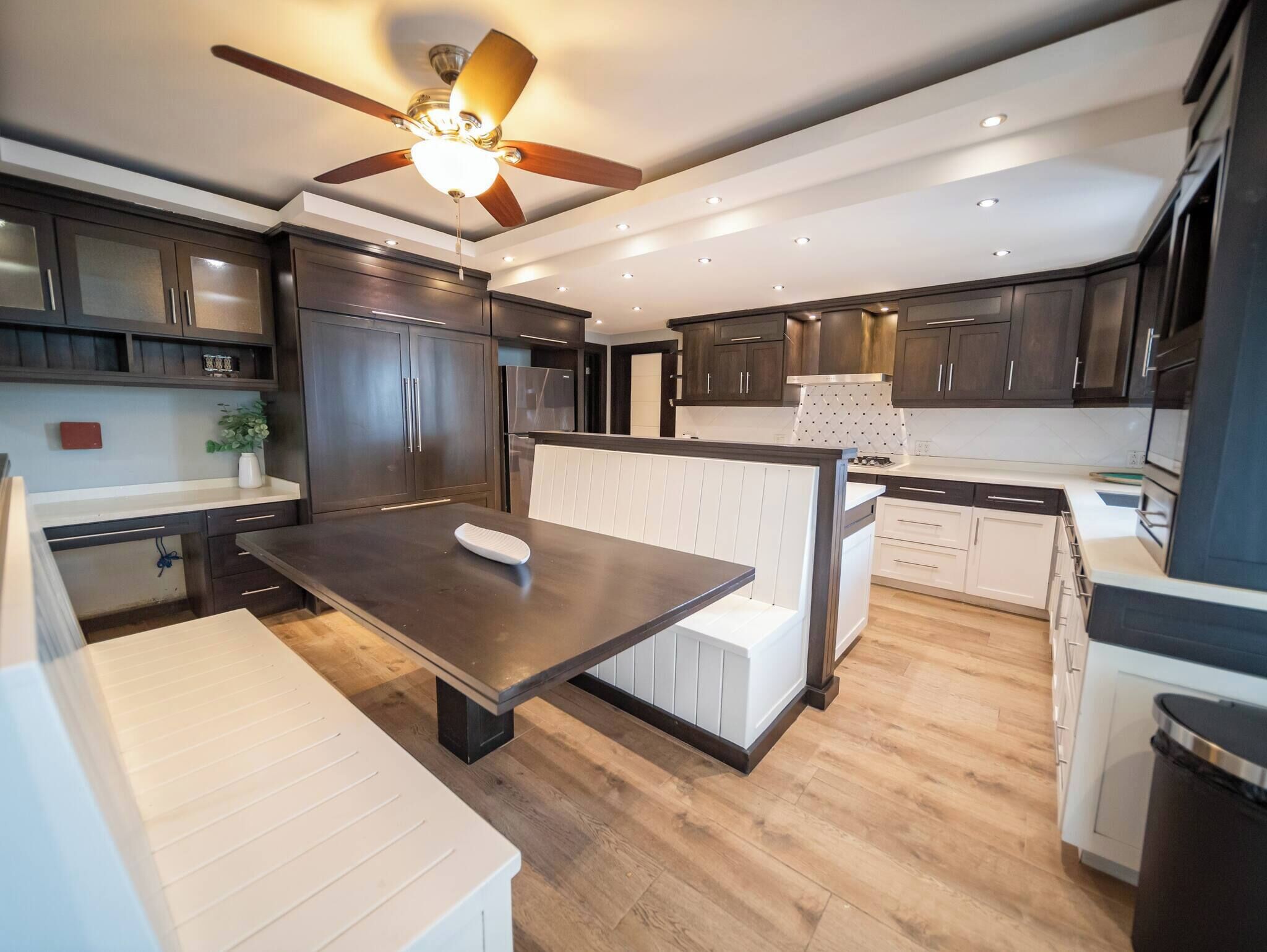 A modern kitchen with dark wood cabinets, a central island, a ceiling fan, and recessed lighting.