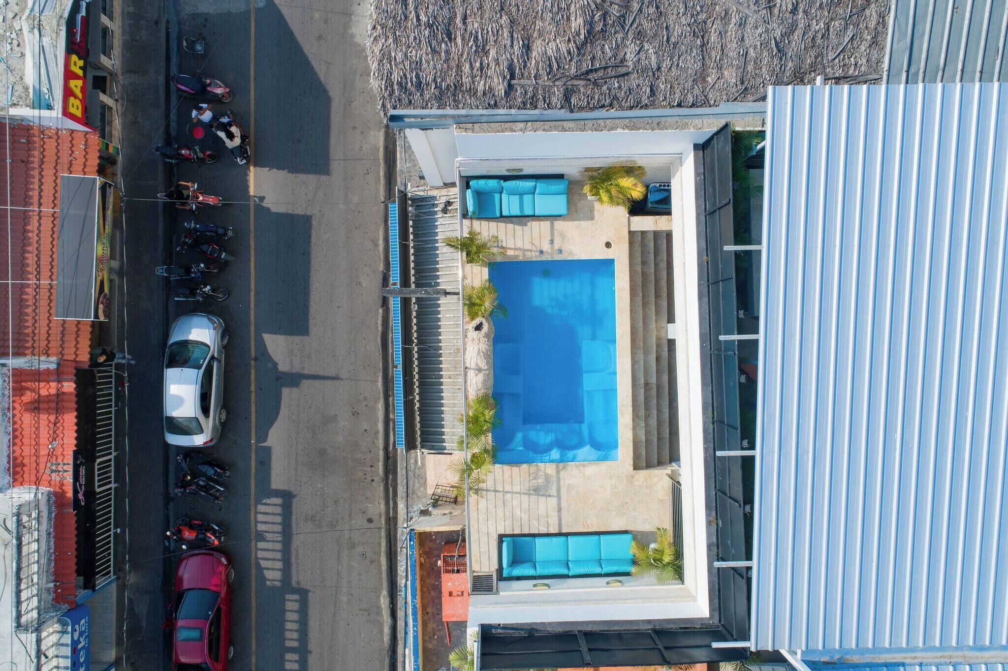 Vista aérea de una propiedad con piscina, zona de estar cubierta al aire libre y aparcamiento con varios coches.