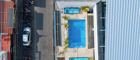 Vista aérea de una propiedad con piscina, zona de estar cubierta al aire libre y aparcamiento con varios coches.