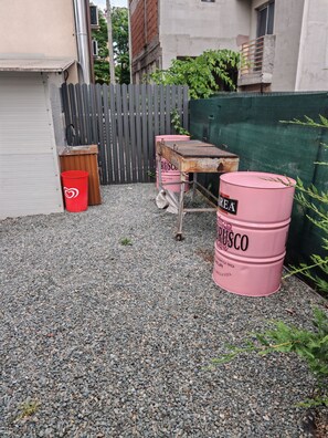 A gravel yard with a wooden table, a metal stool, and two pink barrels labeled "RUSCO".