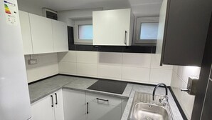 Una cocina compacta con armarios blancos, un lavamanos de acero inoxidable y un suelo de baldosas negras.