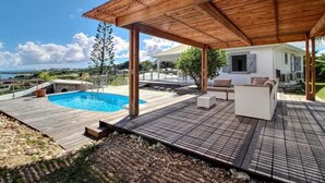 Une terrasse en bois avec une piscine, du mobilier d’extérieur et un espace abrité.