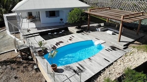 Une maison avec une piscine, un patio couvert et un petit jardin.