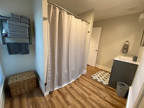 A bathroom with a shower curtain, a sink, a small trash can, and a checkered mat on the floor.