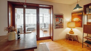 Un salon moderne avec un plancher en bois, une table à manger, un canapé et une lampe. Il y a une affiche au mur et une bibliothèque.