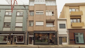 Une rangée d’immeubles à trois étages, dotés de devantures de magasins, dont l’un, bien visible, porte le nom de « Angel Optic ».