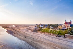 A coastal town with a prominent red building with towers, a sandy beach, and a calm sea. - Un Cadre Exceptionnel au Cœur de la Baie de Somme ! (Le Crotoy)