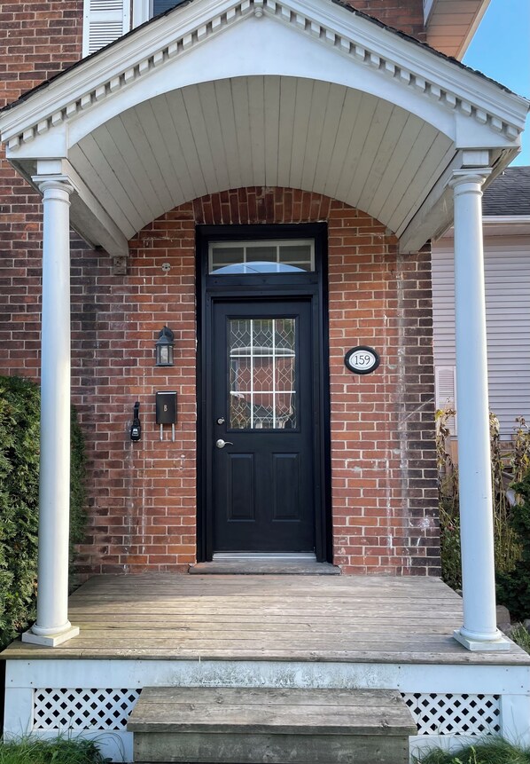 A brick house with a black front door, a porch with white columns, and a mailbox.