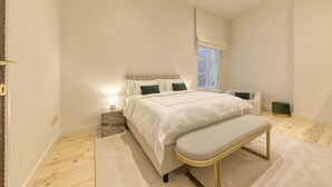 Ein Schlafzimmer mit einem großen Bett, Nachttischen, einer Bank, einem Fenster und einem kleinen Stuhl.