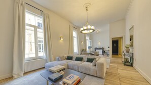 Ein geräumiges Wohnzimmer mit einer großen Couch, einem Couchtisch mit Büchern und einer Kristallleuchtre.