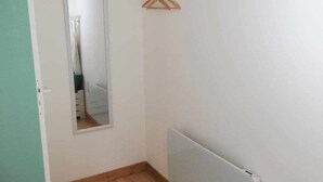 Ein Zimmer mit Holzboden, weißen Wänden, einem Holzbalken an der Decke, einem Heizkörper und einem Spiegel an der Wand.