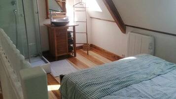 A bedroom with a sloped ceiling, a wooden dresser, a mirror, a radiator, and a bed with a patterned blanket.