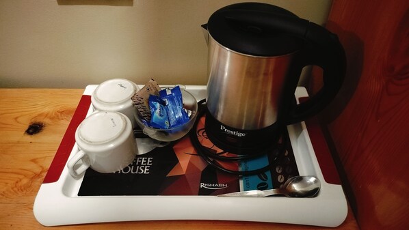A coffee maker, two cups, a packet of coffee, and a spoon on a tray.