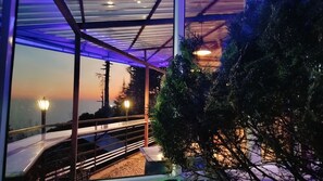 A modern building with a glass facade, outdoor seating area, and a view of the sunset.
