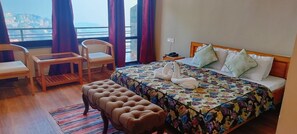 A hotel room with a bed, a wooden bench, a small table, and a chair.