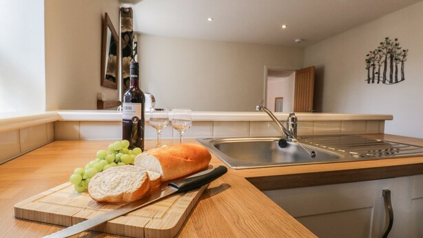 A kitchen with a wooden countertop, a cutting board with bread and grapes, a knife, a wine bottle, and two glasses. - La'l Tethera (Ambleside)