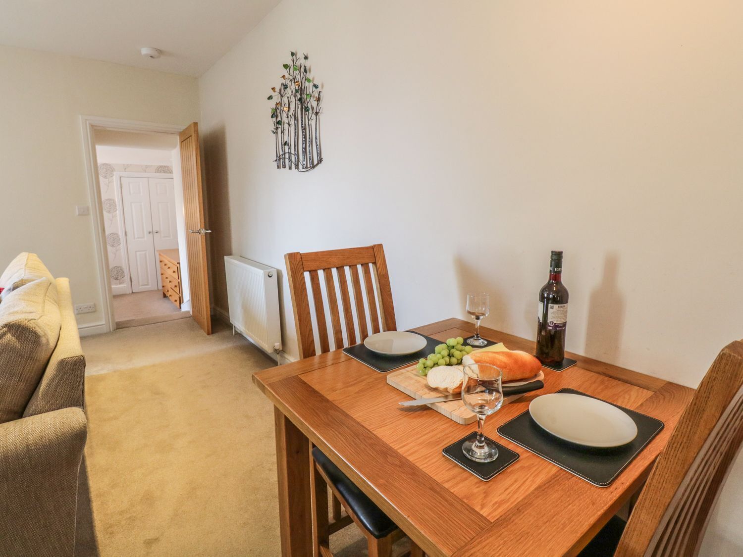 A dining area with a wooden table set for two, a bottle of wine, and a loaf of bread.