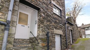 A stone building with a white door, a window, and a small porch area. - La'l Tethera (Ambleside)