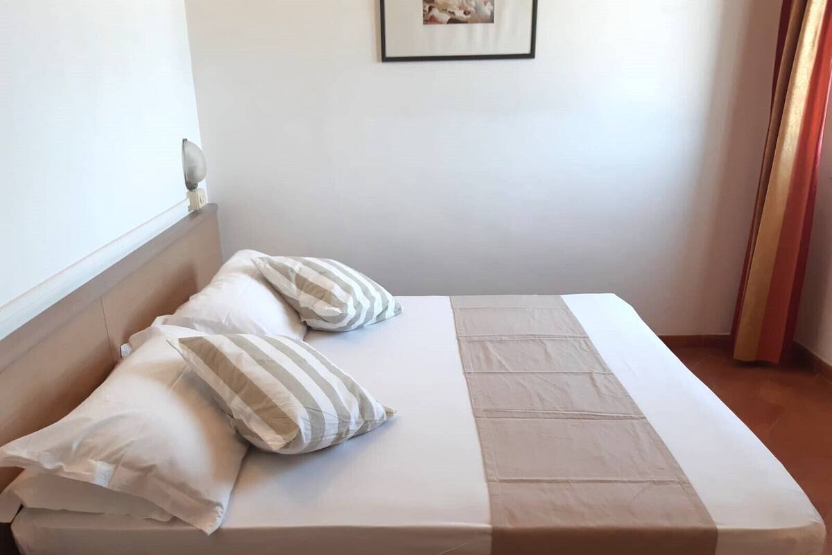 Una cama individual con dos almohadas, una pared lisa y un cuadro enmarcado encima.