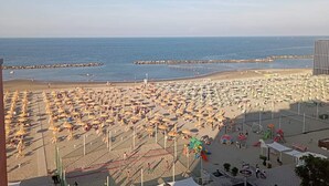 A beach with numerous umbrellas and sun loungers, a volleyball net, and a pier in the background. - Hotel Salsedine  (Rimini)
