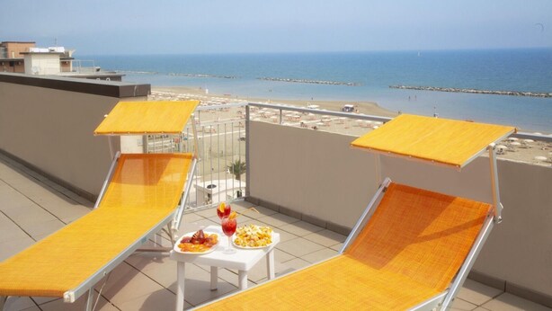 A balcony with two sun loungers and a table with food and drinks, overlooking a beach and the sea. - Hotel Salsedine  (Rimini)