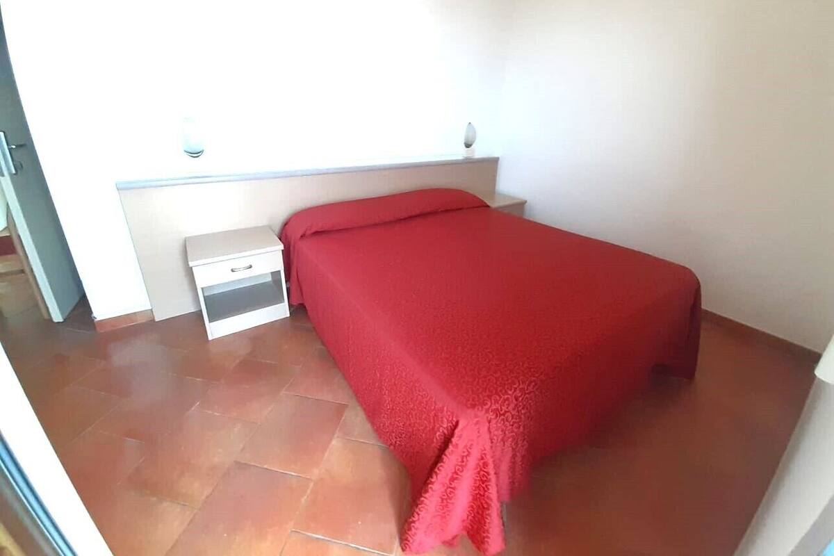 Un dormitorio pequeño con una cama individual, una mesita de noche y una pared blanca.