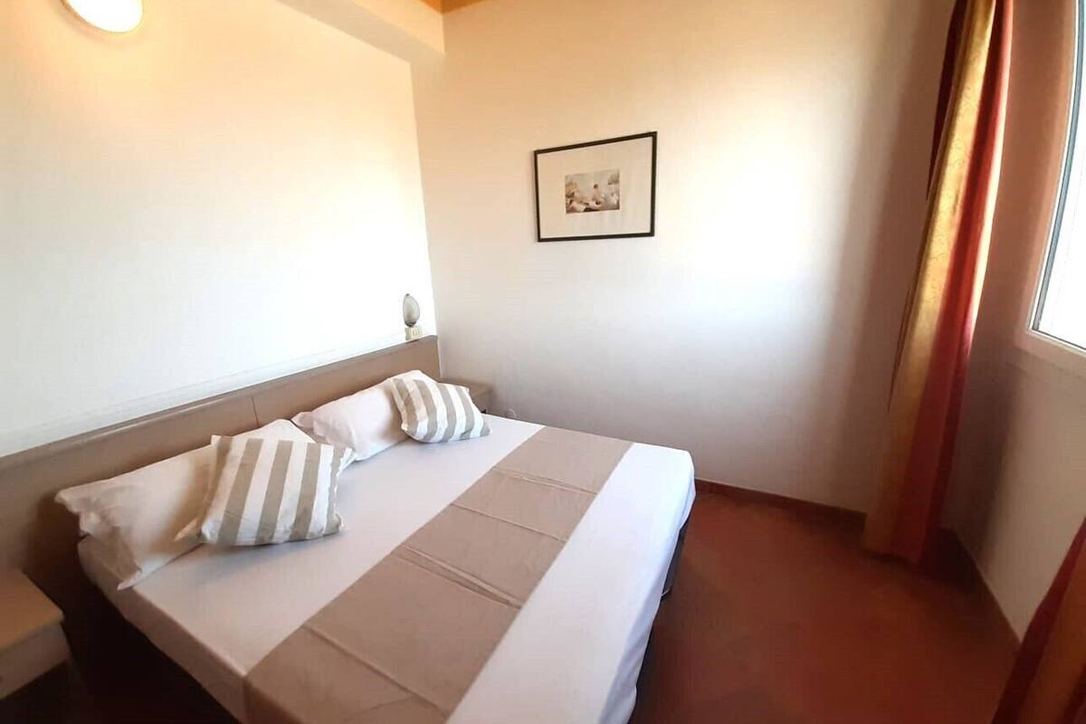Habitación de hotel con cama, mesita de noche, un cuadro enmarcado en la pared y una ventana con cortinas.