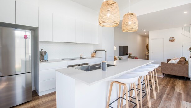 A modern kitchen with white cabinetry, a stainless steel refrigerator, a built-in oven, and a large island with bar stools. - Burra Beachy - Pet Friendly - 5 Mins Walk to Beach (Culburra Beach)