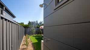 A modern outdoor shower with a metal roof, a wooden fence, and a grassy area with a red and white umbrella. - Burra Beachy - Pet Friendly - 5 Mins Walk to Beach (Culburra Beach)
