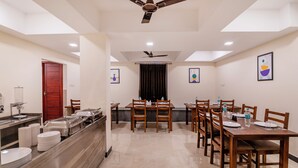A hotel dining area with a buffet setup, multiple dining tables, ceiling fans, and artwork on the walls. - Treebo Rakshitha (Chennai)