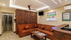 A modern hotel lobby with a sofa, a reception desk, a ceiling fan, and a wall sign. - Treebo Rakshitha (Chennai)