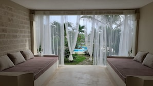 A room with a large window, a bed with a headboard, and a view of a pool and greenery outside. - Giorgia HouseLuxurious Watamu beachfront apartment (Contea di Kilifi)
