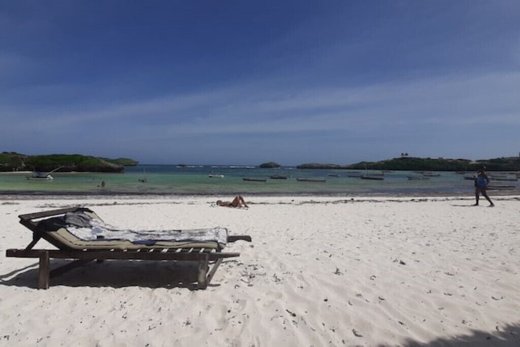 A beach with a single lounge chair and a person walking.