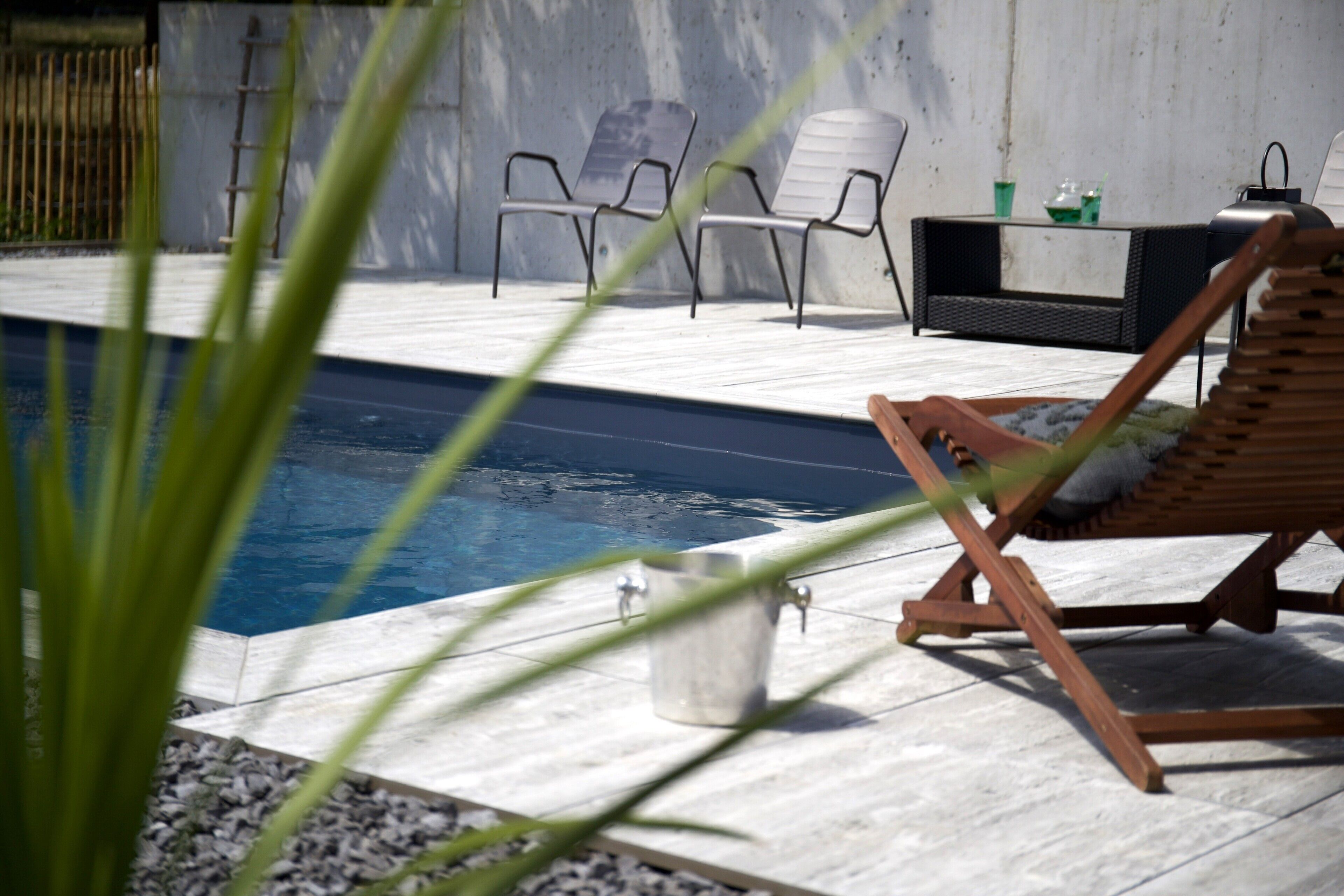 A poolside area with lounge chairs, a small table with a drink, and a metal bucket.