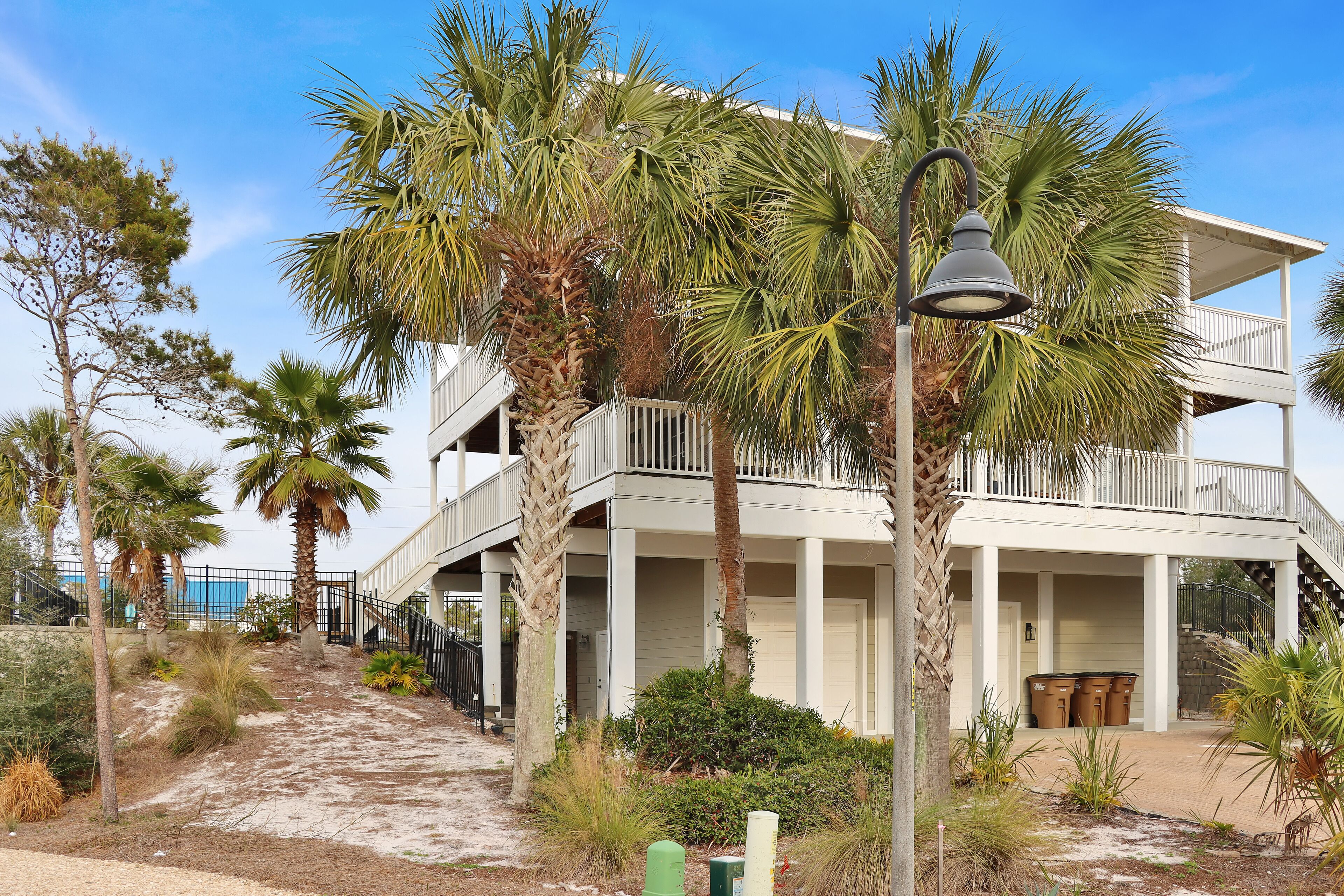 A two-story building with a balcony, surrounded by palm trees and a pathway.