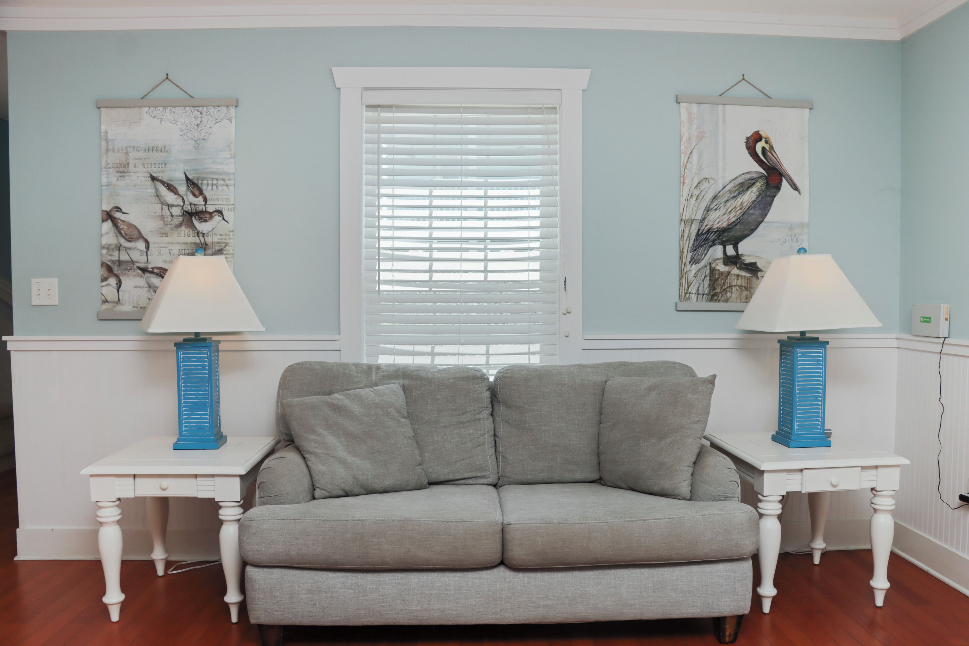 A living room with a grey sofa, two white side tables with lamps, and two wall-mounted bird paintings.