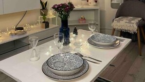 Ruokailutila, jossa on valkoinen pöytä, johon on katettu neljälle, ja pöydän ympärillä on kehystettyjä taideteoksia, koristeellinen tähti ja maljakko kukkineen.