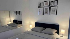 Hotellihuone, jossa on kaksi sänkyä, suuri peili ja seinällä tauluja.