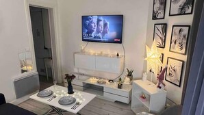 Moderni olohuone, jossa on litteänäyttöinen televisio, ruokapöytä, jossa on jo valmiiksi katettuina lautaset, ja sohva.