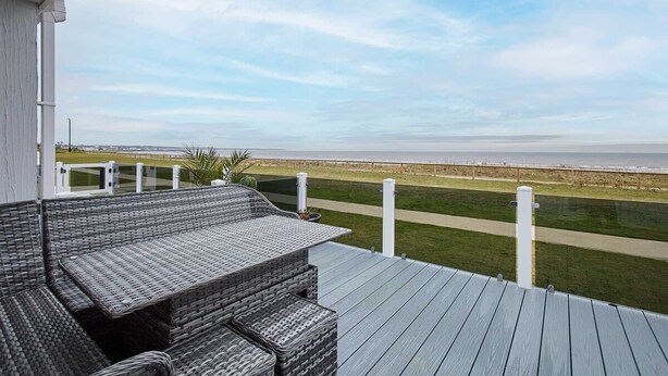 Una terraza con mobiliario de mimbre que da a un espacio verde y una costa lejana.