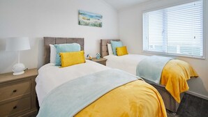 Un dormitorio con dos camas, una mesita de noche con lámpara, un cuadro en la pared y una ventana con persianas.